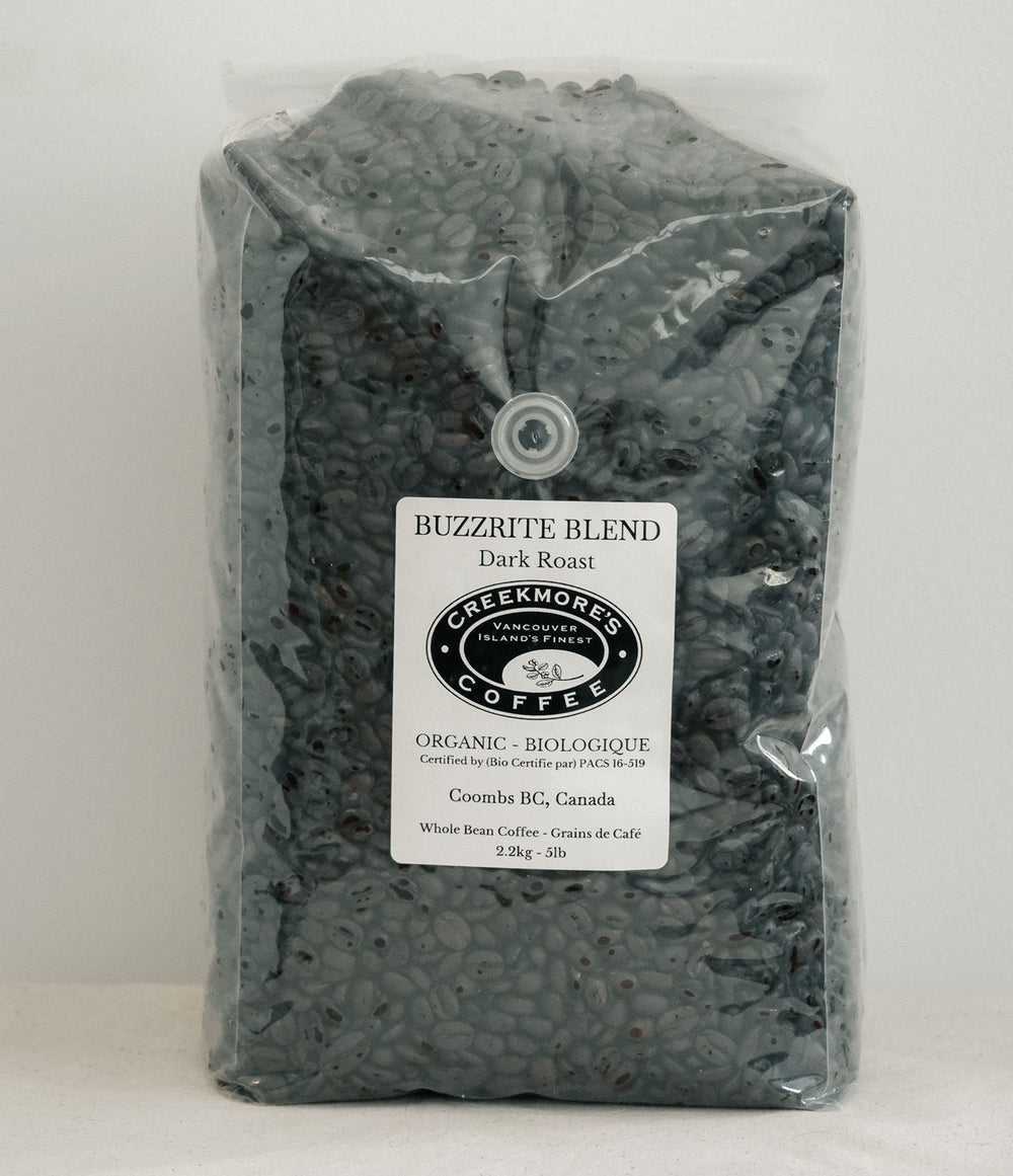A 23kg bag of Creekmore's 'Buzzrite Blend' organic dark roast coffee, shown in a clear plastic bag with a white label on a light gray background.