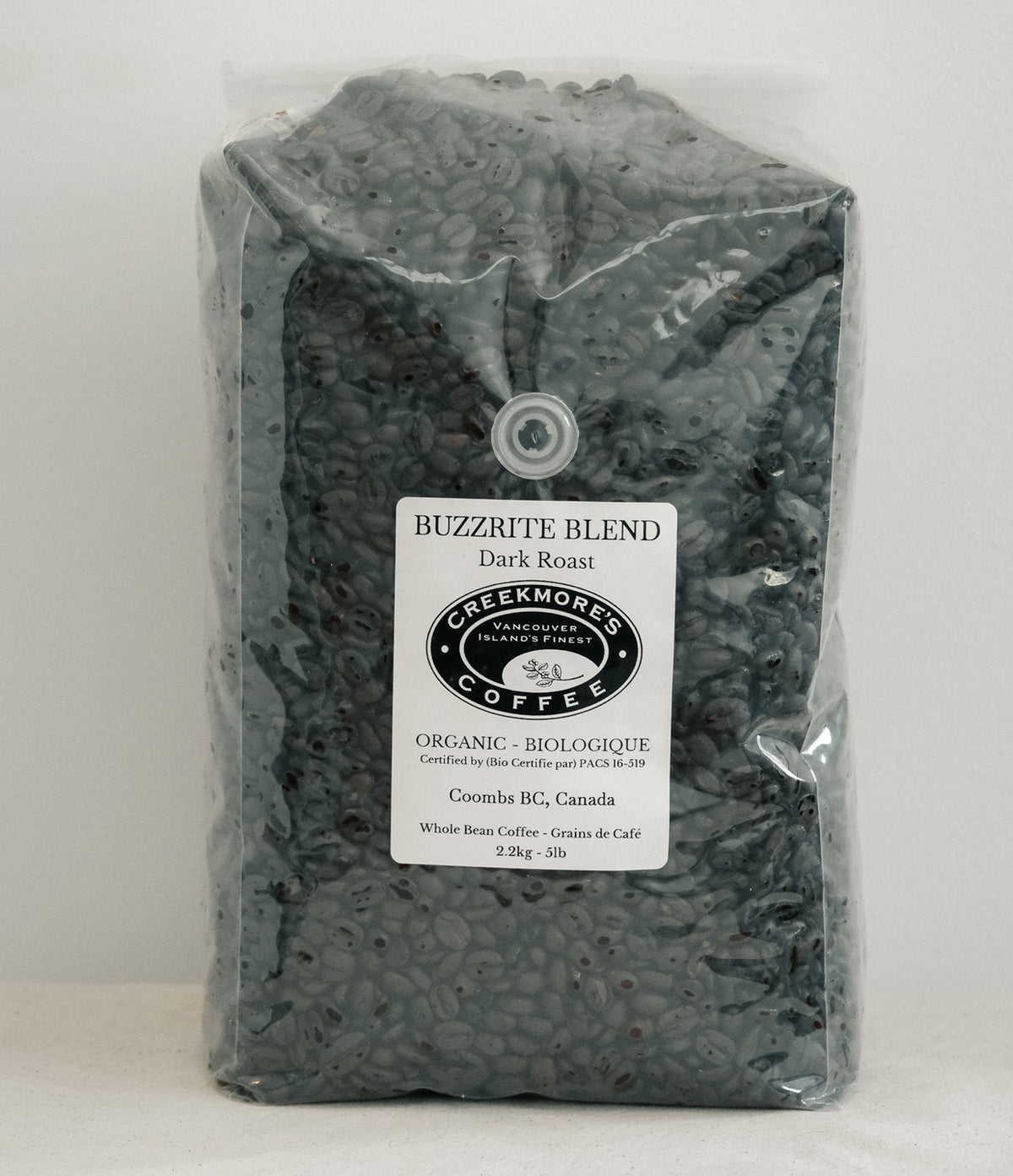 A 23kg bag of Creekmore's 'Buzzrite Blend' organic dark roast coffee, shown in a clear plastic bag with a white label on a light gray background.