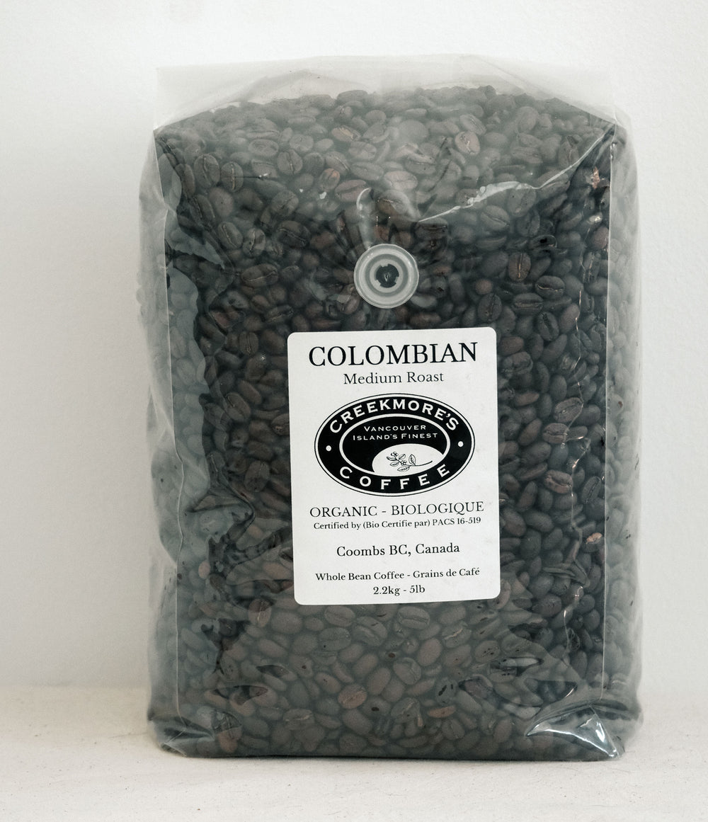 A clear plastic bag filled with dark roasted coffee beans, featuring a white label that reads 'COLOMBIAN Medium Roast' and the 'Creekmori's Coffee' logo.