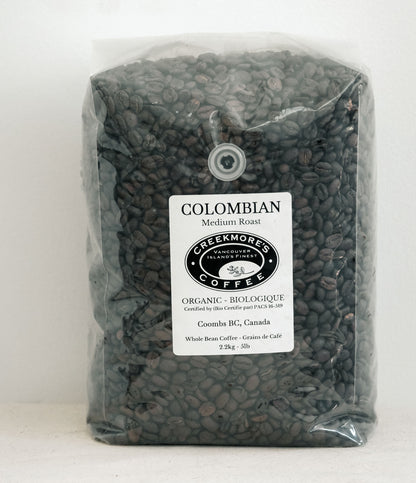 A clear plastic bag filled with dark roasted coffee beans, featuring a white label that reads 'COLOMBIAN Medium Roast' and the 'Creekmori's Coffee' logo.