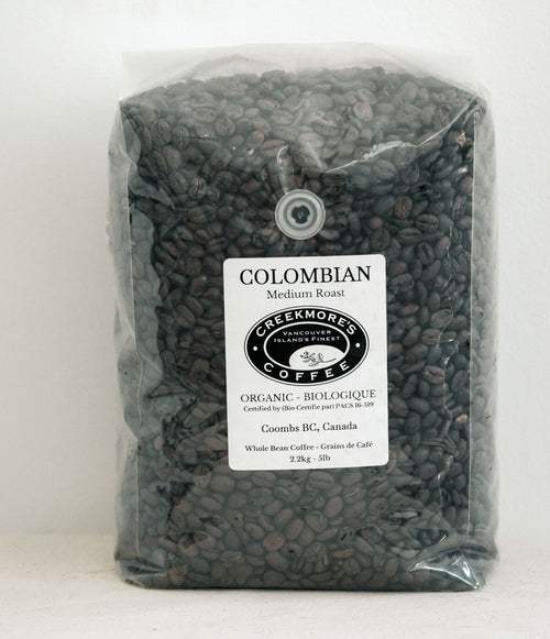 A clear plastic bag filled with dark roasted coffee beans, featuring a white label that reads 'COLOMBIAN Medium Roast' and the 'Creekmori's Coffee' logo.