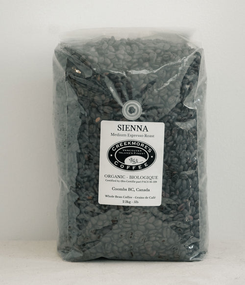 A clear plastic bag filled with dark brown coffee beans, featuring a white label for Creekmore Coffee's Sierra Medium Espresso Roast.